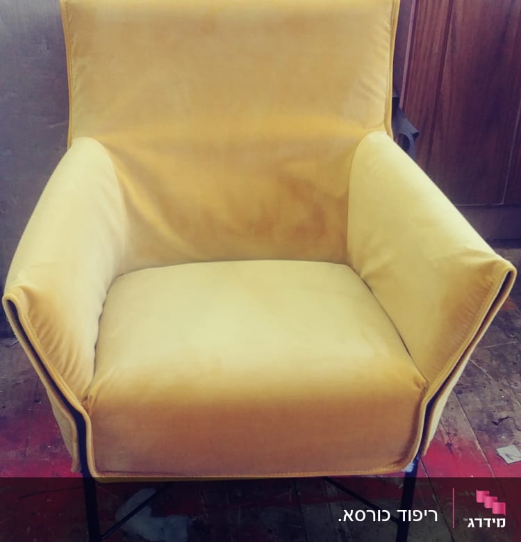 כורסה מרופדת בצבע צהוב על רצפת עץ